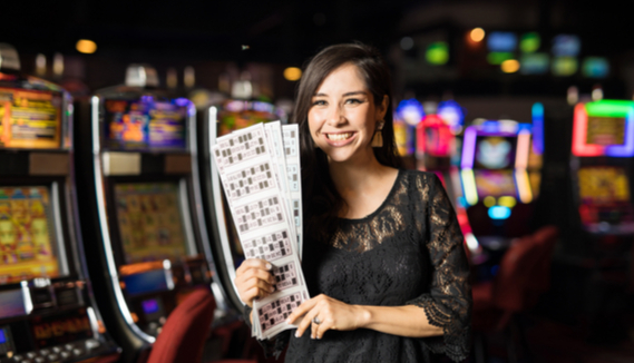 smiling woman holding bingo cards standing in a casino with slot machines in the background